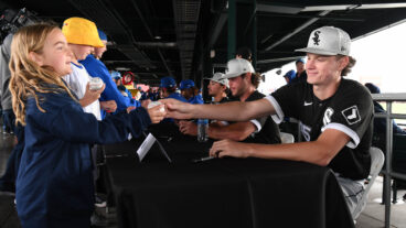 Top prospect Noah Schultz, a key piece of the Chicago White Sox rebuild, signs a baseball for a young fan during a rain delay prior to the game between the Chicago White Sox and the Chicago Cubs.