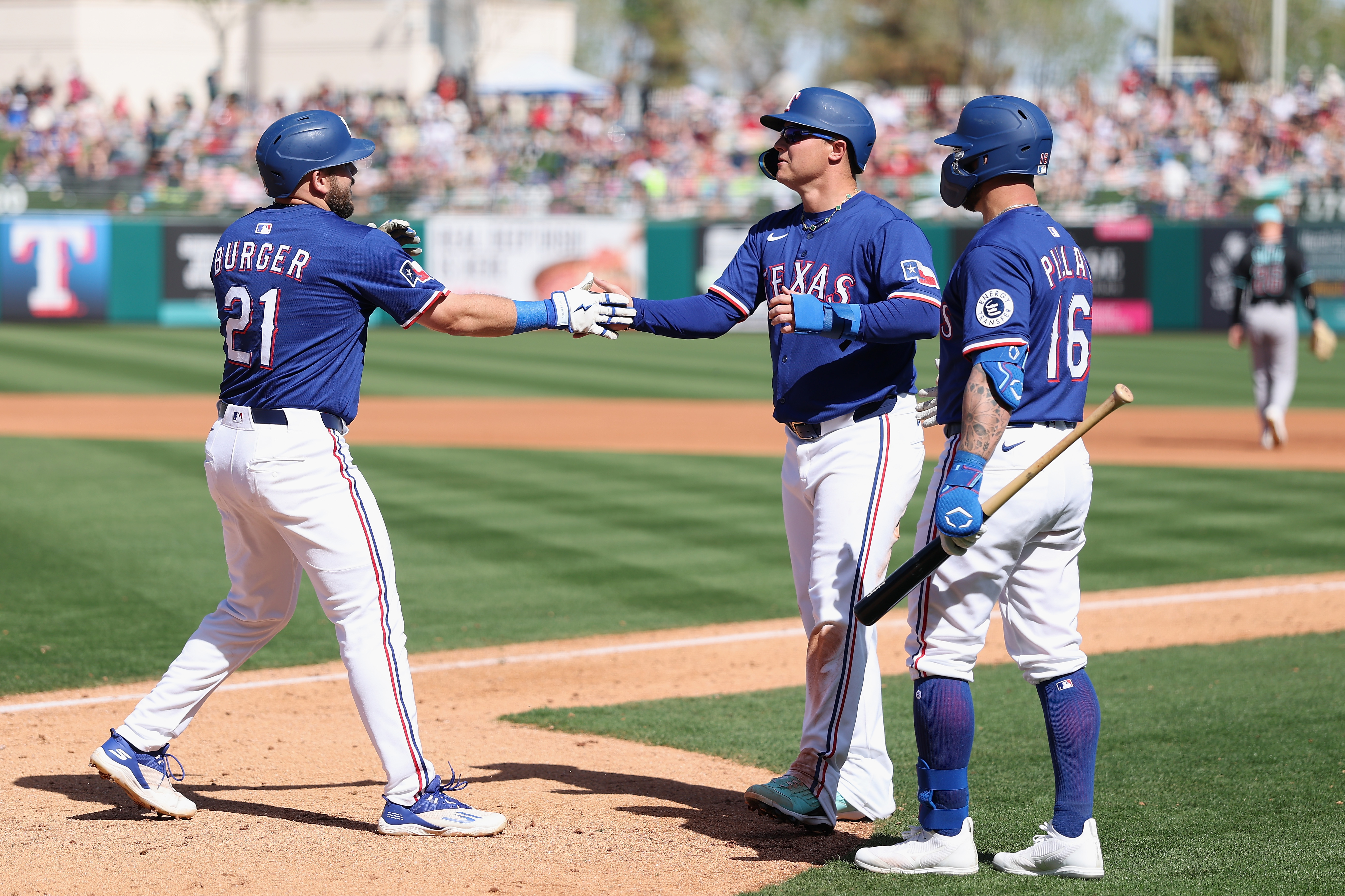 SURPRISE, ARIZONA - MARCH 02: Jake Burger #21 of the Texas Rangers high fives Joc Pederson #4 and Kevin Pillar #16 after hitting a two-run home run against the Arizona Diamondbacks during the fourth inning of the MLB game at Surprise Stadium on March 02, 2025 in Surprise, Arizona. (Photo by Christian Petersen/Getty Images)